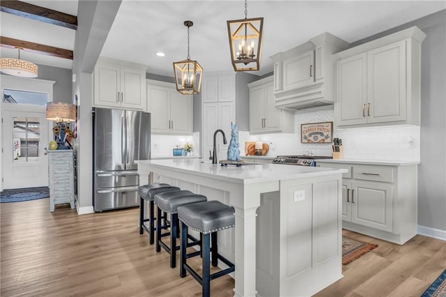 kitchen with a breakfast bar, light wood-style flooring, freestanding refrigerator, a sink, and an island with sink