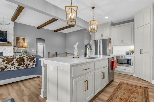 kitchen with light wood finished floors, arched walkways, open floor plan, stainless steel appliances, and a sink