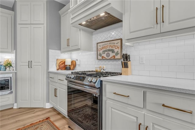 kitchen featuring white cabinetry, light wood-style floors, stainless steel gas range, backsplash, and custom range hood