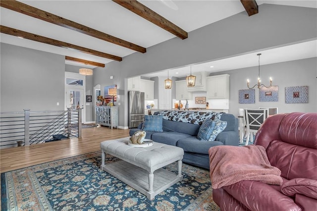 living area with a notable chandelier, lofted ceiling with beams, baseboards, and wood finished floors