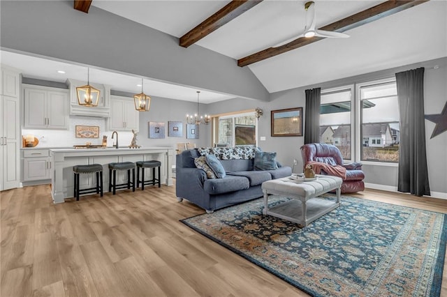 living room with lofted ceiling with beams, light wood-type flooring, baseboards, and ceiling fan with notable chandelier