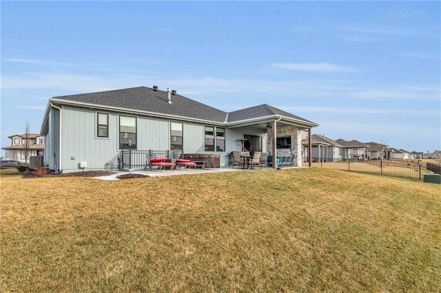 rear view of house with a shingled roof, a patio area, fence, and a lawn