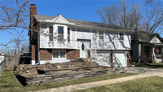 bi-level home featuring brick siding, fence, concrete driveway, a chimney, and a garage