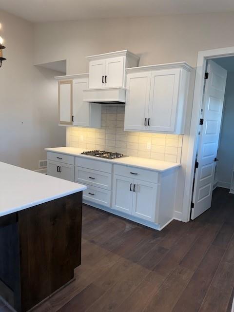 kitchen with dark wood-style floors, stainless steel gas cooktop, light countertops, and backsplash