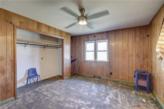 unfurnished bedroom featuring visible vents, wooden walls, a ceiling fan, and a closet