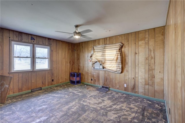 unfurnished room featuring wood walls, a ceiling fan, and baseboards