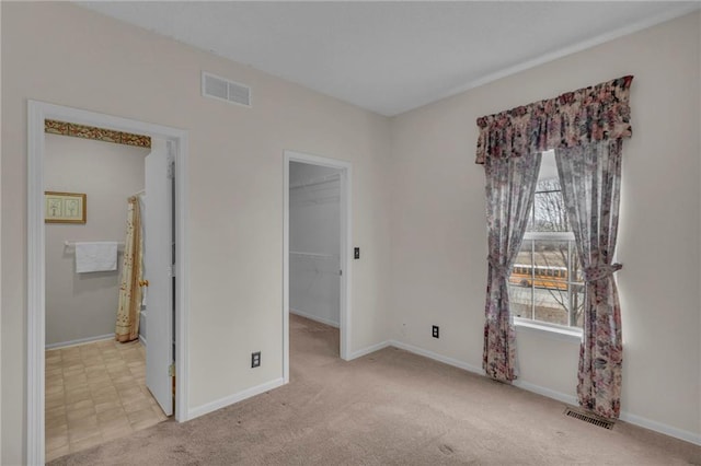 unfurnished bedroom with carpet flooring, a walk in closet, multiple windows, and visible vents