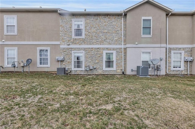 rear view of property featuring central air condition unit, a lawn, and stucco siding