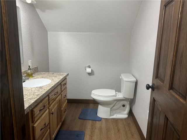 half bath with toilet, wood finished floors, baseboards, vanity, and a textured wall