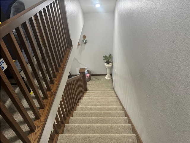 stairway featuring baseboards, carpet, and a textured wall