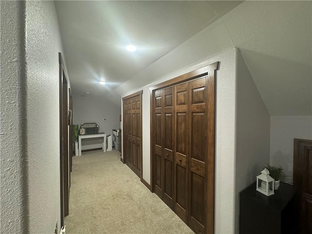 hall featuring light colored carpet, a textured wall, and vaulted ceiling