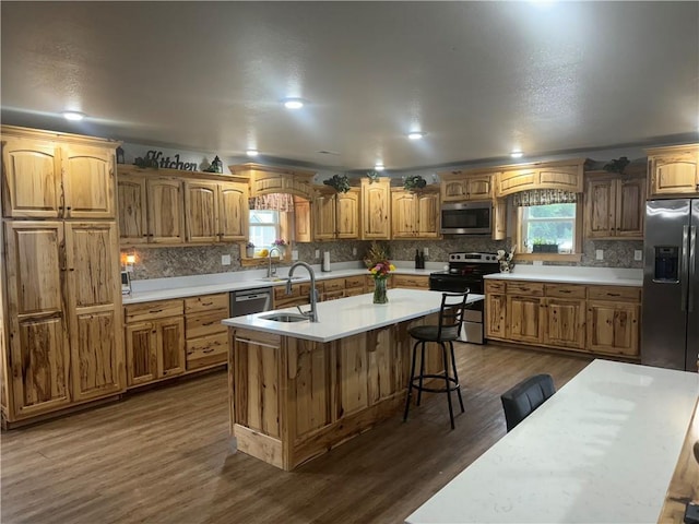 kitchen with backsplash, light countertops, dark wood-style flooring, stainless steel appliances, and a kitchen island with sink