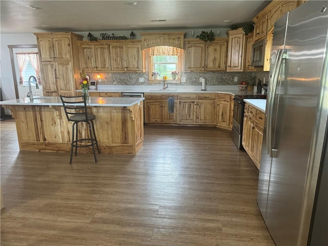 kitchen with light countertops, freestanding refrigerator, dark wood-style floors, black electric range oven, and a kitchen island with sink