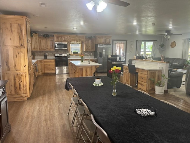 kitchen featuring wood finished floors, visible vents, a center island with sink, stainless steel appliances, and open floor plan