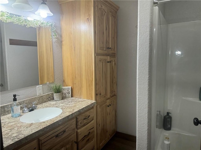 full bath featuring vanity, walk in shower, and a textured wall