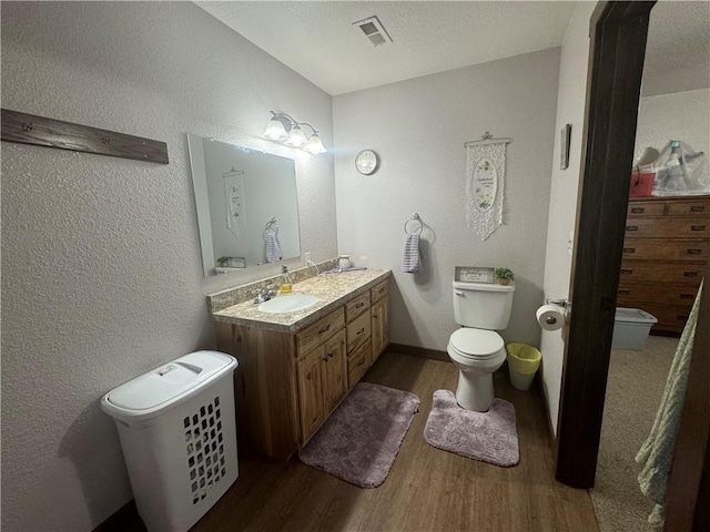 bathroom with visible vents, toilet, wood finished floors, a textured wall, and vanity