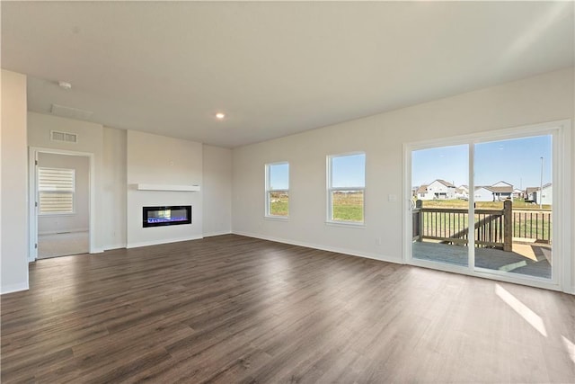 unfurnished living room featuring dark wood-type flooring, a glass covered fireplace, visible vents, and baseboards