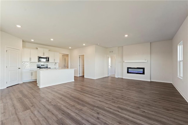 unfurnished living room featuring recessed lighting, baseboards, dark wood finished floors, and a glass covered fireplace