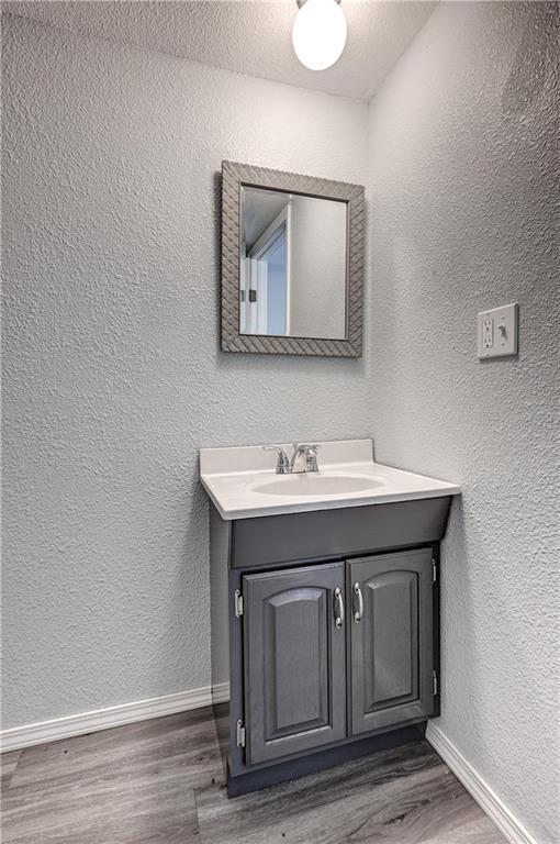 511 N E Ave, Columbus, KS 66725 - bathroom with a textured wall, baseboards, wood finished floors, and vanity