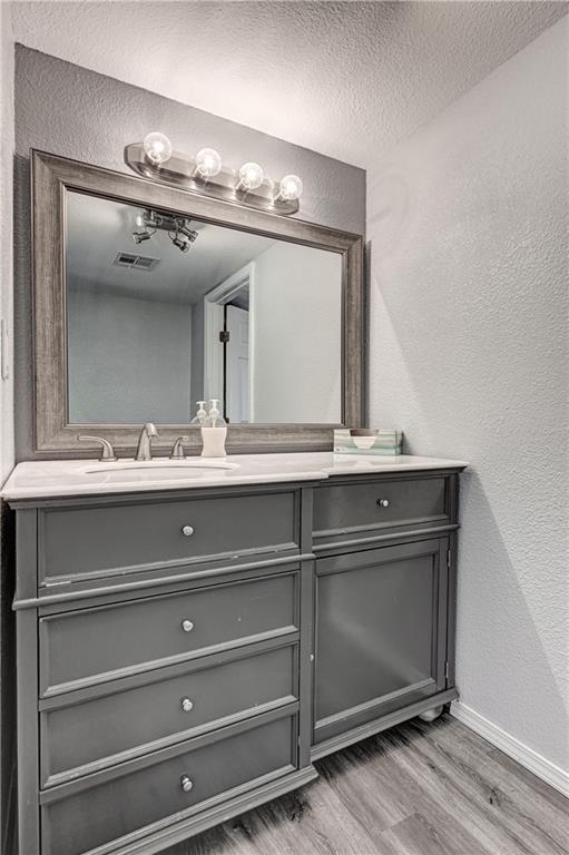511 N E Ave, Columbus, KS 66725 - bathroom featuring wood finished floors, baseboards, a textured wall, vanity, and a textured ceiling