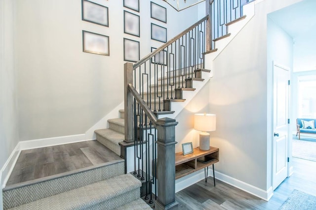 stairway featuring a high ceiling, wood finished floors, and baseboards