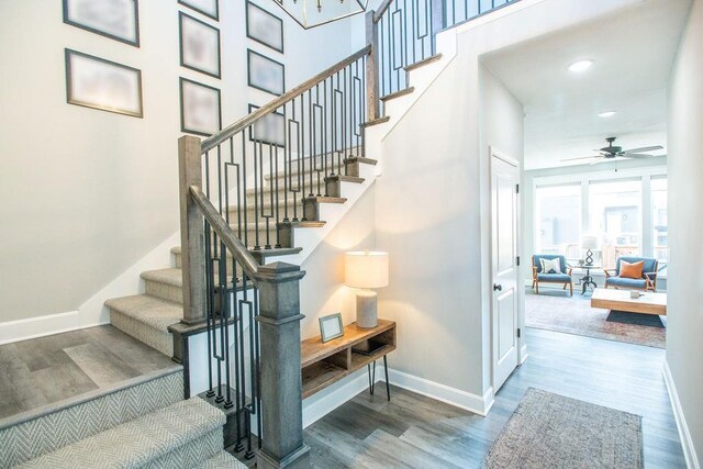 stairway featuring baseboards, a towering ceiling, ceiling fan, wood finished floors, and recessed lighting