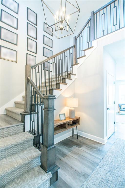 stairway featuring a notable chandelier, a towering ceiling, baseboards, and wood finished floors