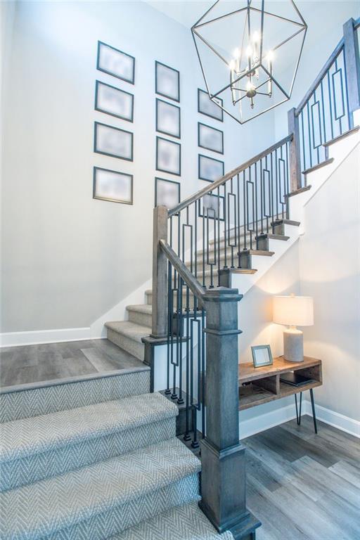 staircase with a towering ceiling, a notable chandelier, baseboards, and wood finished floors