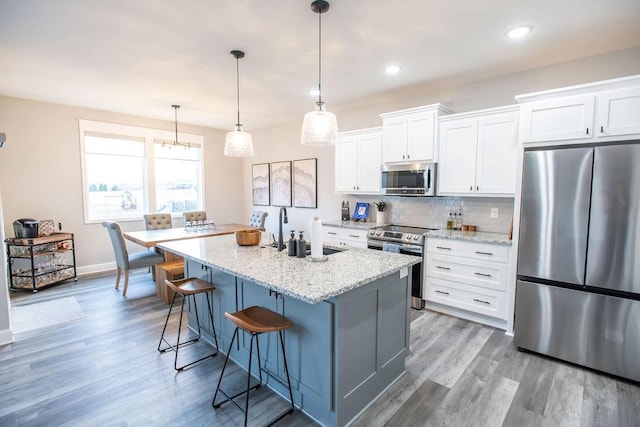 kitchen featuring light wood finished floors, tasteful backsplash, a breakfast bar area, a kitchen island with sink, and stainless steel appliances