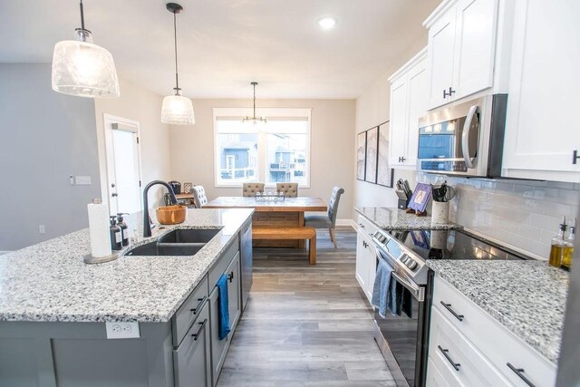 kitchen with light wood finished floors, white cabinets, decorative backsplash, stainless steel appliances, and a sink