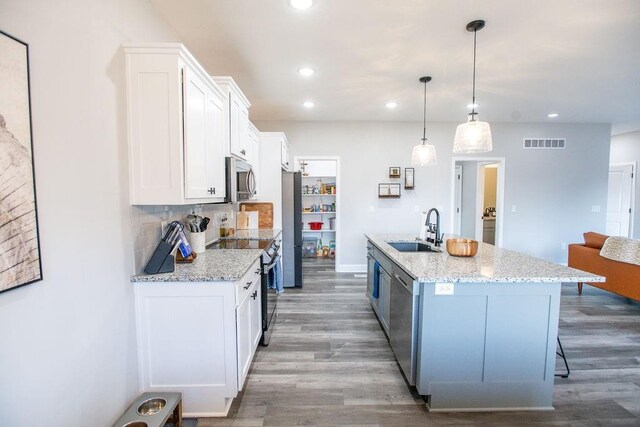 kitchen with stainless steel appliances, visible vents, white cabinets, a sink, and wood finished floors