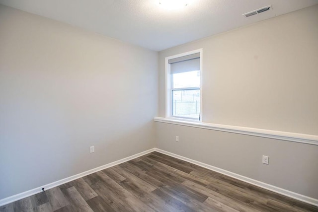 spare room with dark wood-style flooring, visible vents, and baseboards