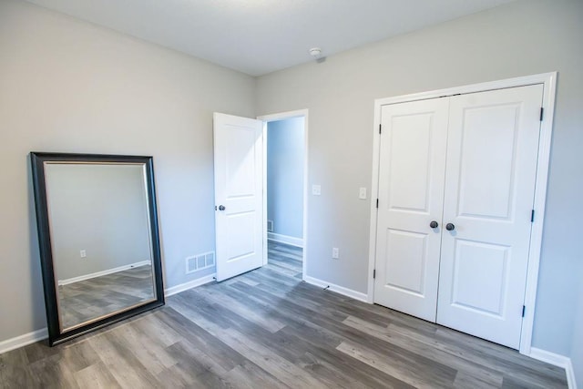 unfurnished bedroom with a closet, wood finished floors, visible vents, and baseboards