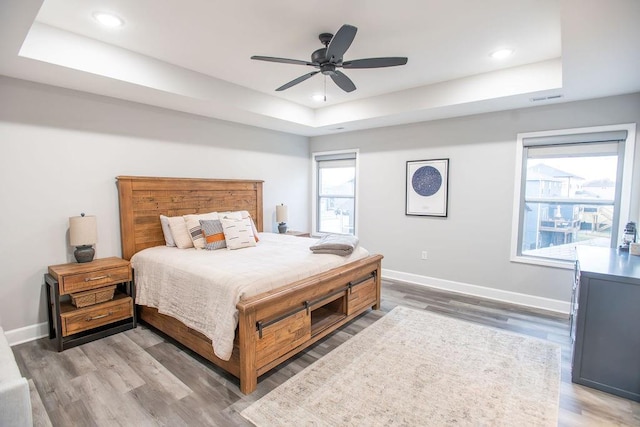 bedroom featuring wood finished floors, a raised ceiling, visible vents, and baseboards