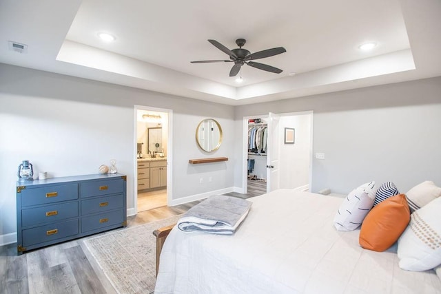 bedroom with light wood-type flooring, a tray ceiling, a walk in closet, and visible vents