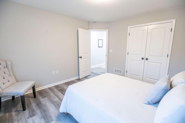 bedroom with a closet, wood finished floors, visible vents, and baseboards