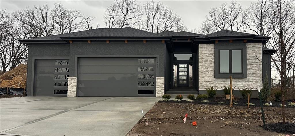 prairie-style house featuring a garage, stone siding, driveway, and stucco siding