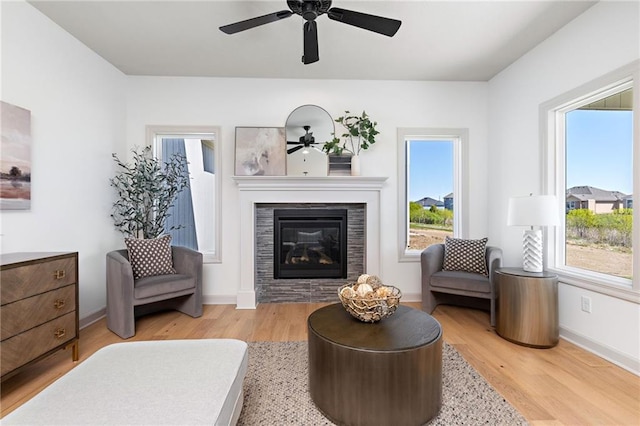 sitting room featuring a ceiling fan, a glass covered fireplace, baseboards, and wood finished floors