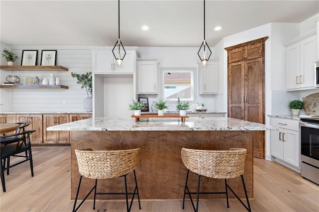 kitchen featuring light wood-type flooring, a center island, white cabinets, and stainless steel range with electric cooktop