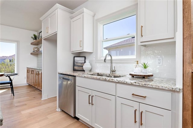 kitchen with white cabinets, light wood-style flooring, light stone counters, stainless steel dishwasher, and a sink