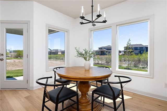 dining space with baseboards, light wood-type flooring, a residential view, and an inviting chandelier