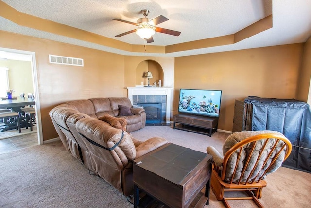 carpeted living area featuring visible vents, a ceiling fan, a textured ceiling, a fireplace, and a raised ceiling