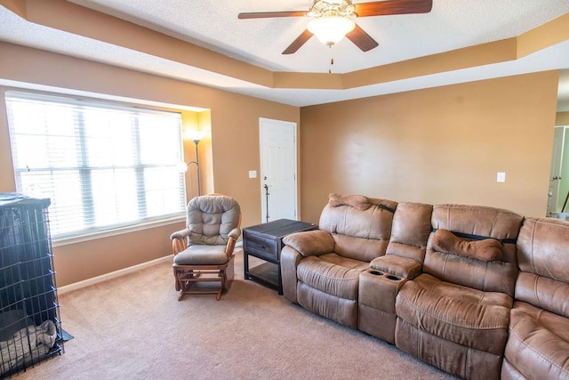 living area with baseboards, ceiling fan, a textured ceiling, a raised ceiling, and carpet flooring