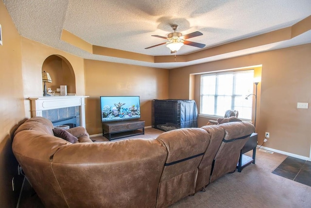 living area featuring a tiled fireplace, a ceiling fan, a tray ceiling, a textured ceiling, and baseboards