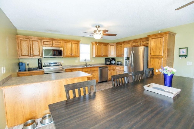 kitchen with ceiling fan, light countertops, appliances with stainless steel finishes, a peninsula, and a sink