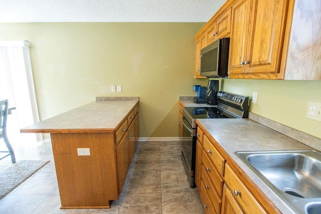 kitchen with a peninsula, a sink, stainless steel appliances, a textured ceiling, and brown cabinets