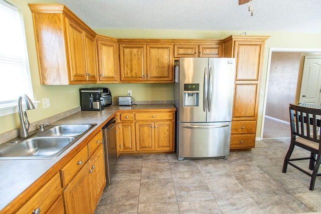 kitchen featuring a sink, a textured ceiling, appliances with stainless steel finishes, and brown cabinetry