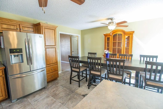 kitchen featuring a textured ceiling, brown cabinetry, stainless steel refrigerator with ice dispenser, and ceiling fan