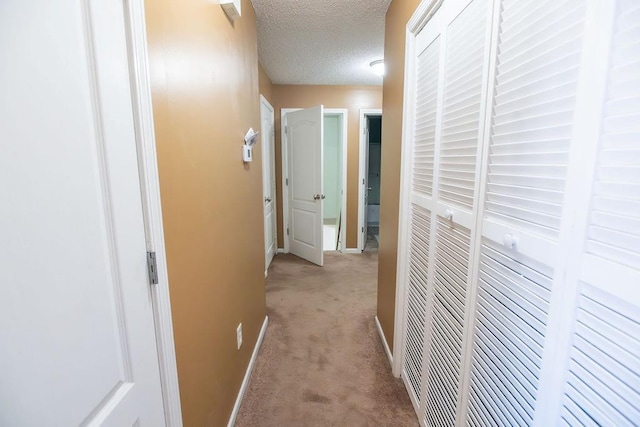 hall featuring light carpet, a textured ceiling, and baseboards