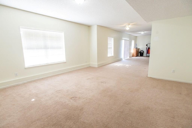 empty room with baseboards, light colored carpet, a ceiling fan, and a textured ceiling